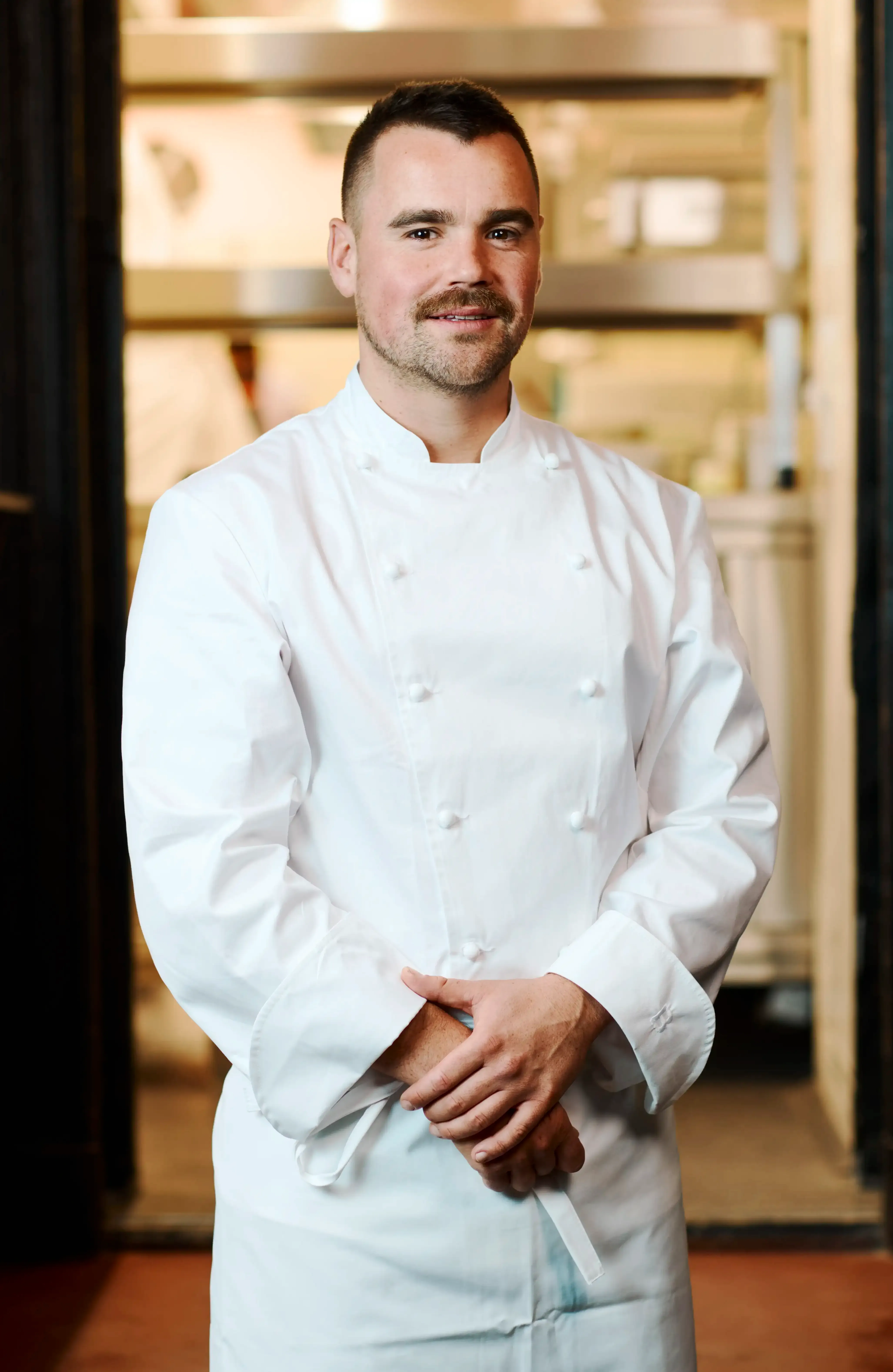 Tobias Beck wearing a chef's outfit standing in front of the kitchen of Claerchens Ballhaus in Berlin
